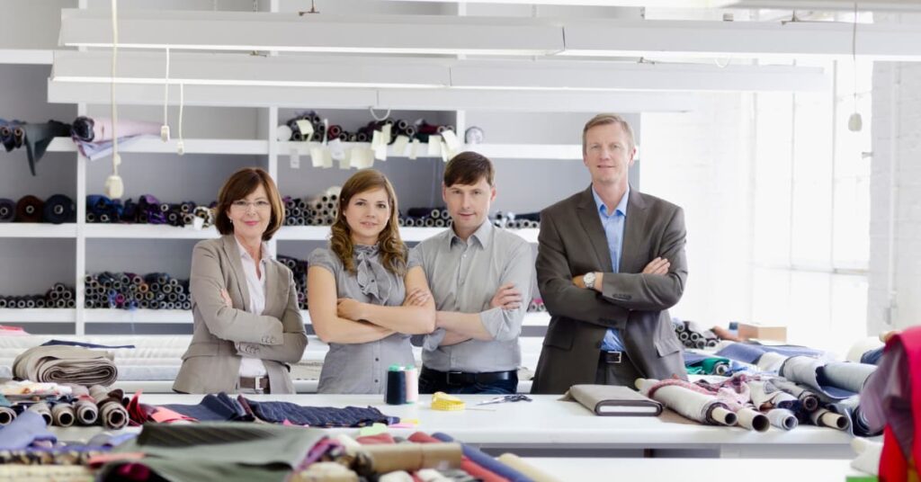 Grupo de empresarios en una empresa textil familiar, posando juntos con actitud profesional frente a mesas con rollos de tela.